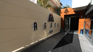 A hotel entrance with a beige wall, a black carpeted path, and a sign reading "AGATE".
