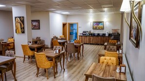 A restaurant with wooden tables and chairs, a coffee station, and artwork on the walls.