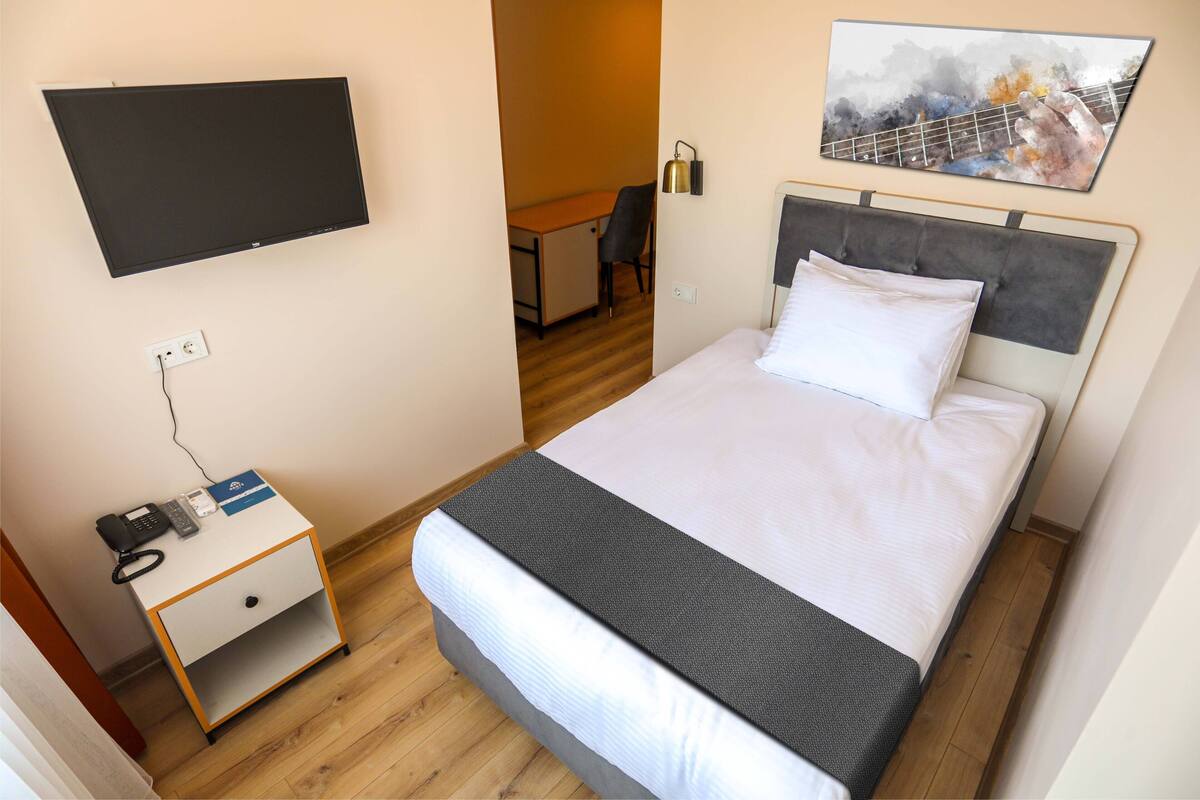 Una camera d'albergo con un letto, una scrivania, una sedia, un televisore montato a parete e un quadro sopra il letto.