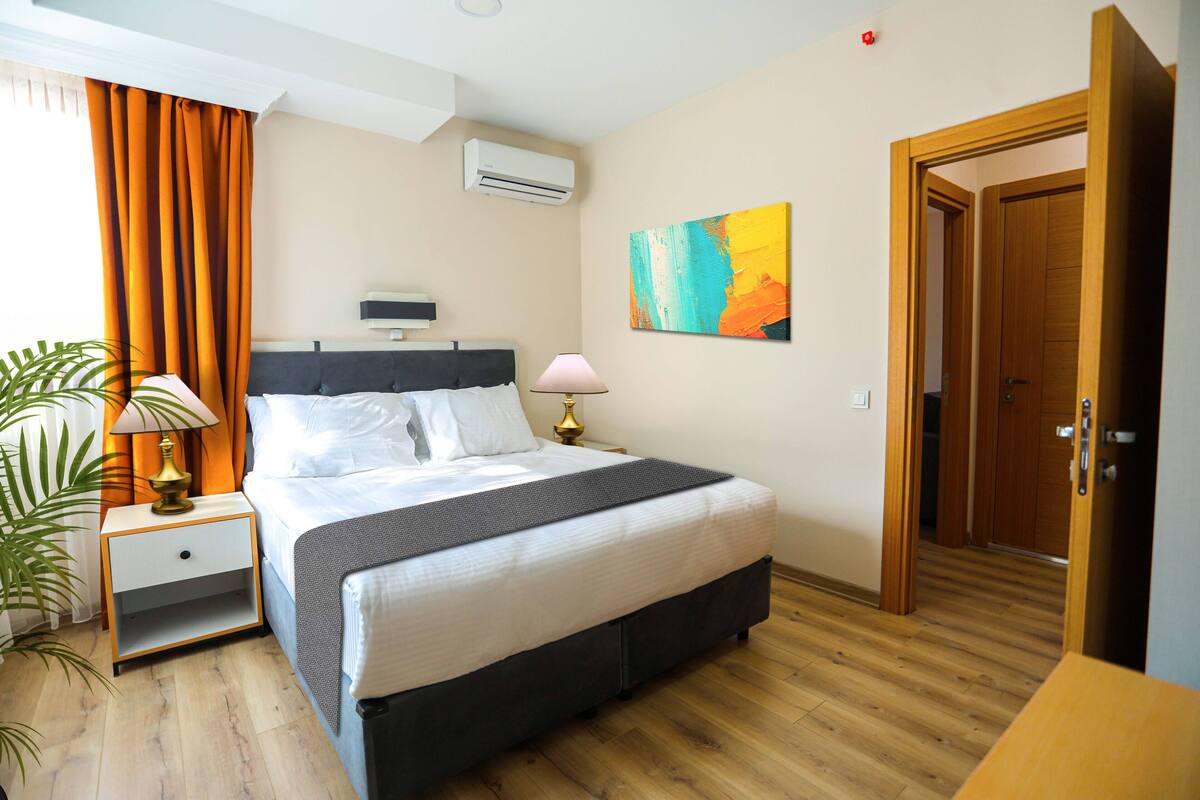 Una camera d'albergo con un letto, un comodino, una lampada, un condizionatore e una porta.
