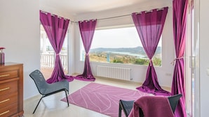 En balkon med lilla gardiner, en stol, et lille bord og udsigt over et landskab.