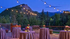 An outdoor patio with round tables, string lights, and floral centerpieces against a mountainous backdrop. - Riverfront Resort and Spa - Luxury Studio Suite: SKI IN / SKI OUT (Avon)