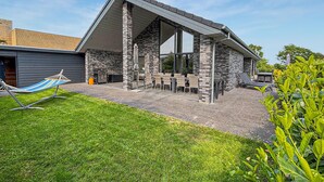 A modern house with a stone facade, a covered patio with outdoor furniture, and a hammock in the yard. - Amazing home in Grenaa with WiFi (Grenaa)