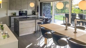 A modern kitchen with dark countertops, a central island, and a dining area with a wooden table and black chairs. - Amazing home in Grenaa with WiFi (Grenaa)