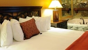 Hotellihuone, jossa on sänky, tyynyjä, yöpöytä, lamppu ja kylpyammeella varustettu kylpyhuone.