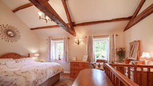 Un dormitorio con una cama grande, vigas de madera, un aparador, una banca y una ventana con cortinas.
