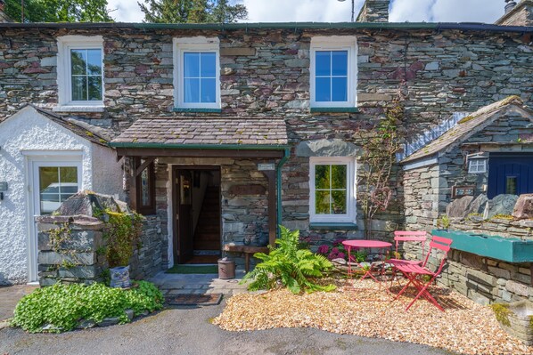 Une petite maison en pierre avec un petit porche, une porte et une fenêtre.