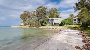 A beachfront property with a modern two-story house, a sandy beach, and clear waters. - Pelican Sands, 3/83 Soldiers Point Rd - stunning waterfront unit, magical views & air conditioning (Soldiers Point)