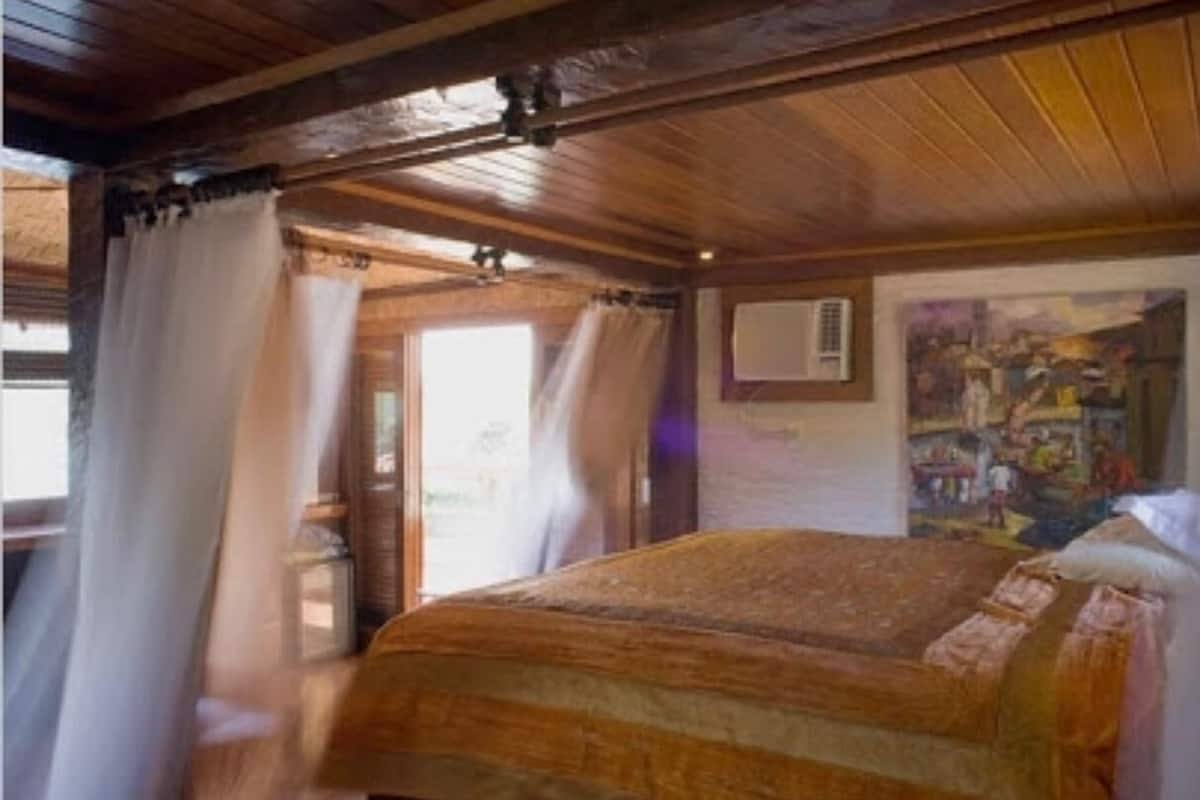 A wooden room with a bed, curtains, and a painting on the wall.
