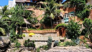 Un edificio costero con fachada de piedra, un elemento acuático visible y abundante vegetación.