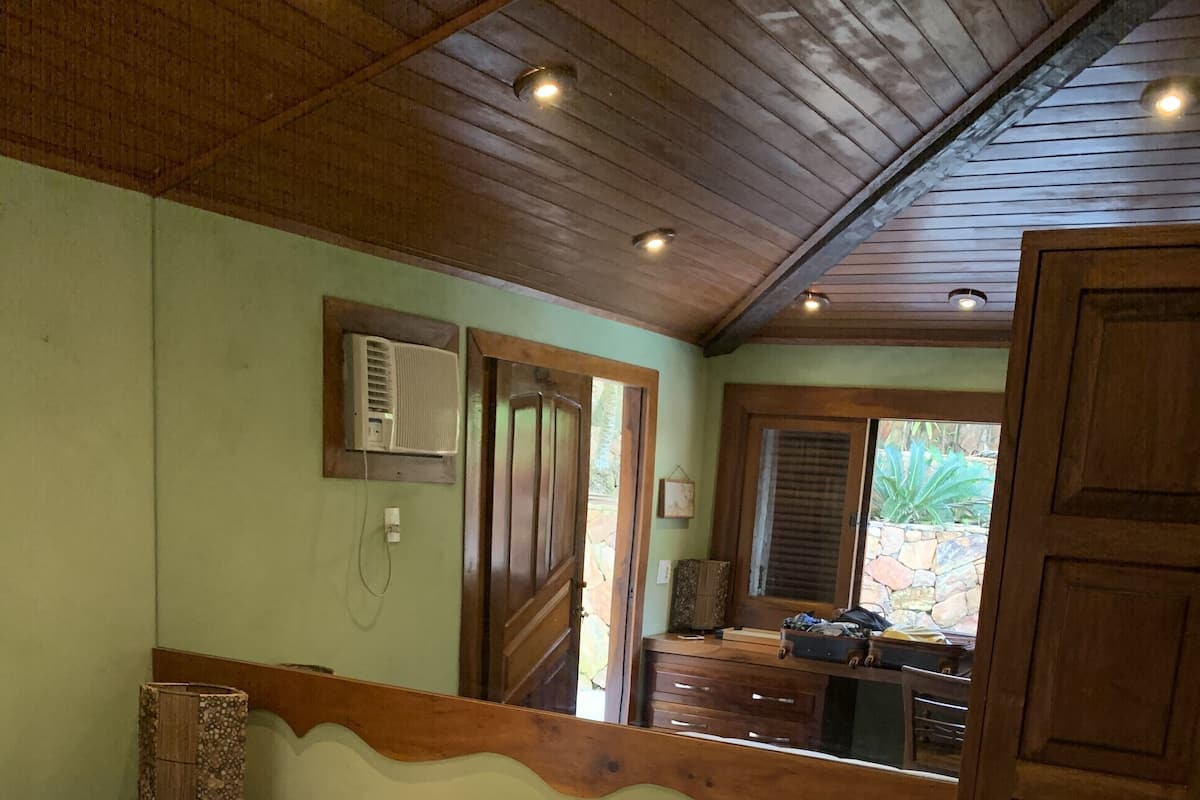 A bedroom with a bed, a wooden headboard, a nightstand, a dresser, and a window with a view of the outdoors.