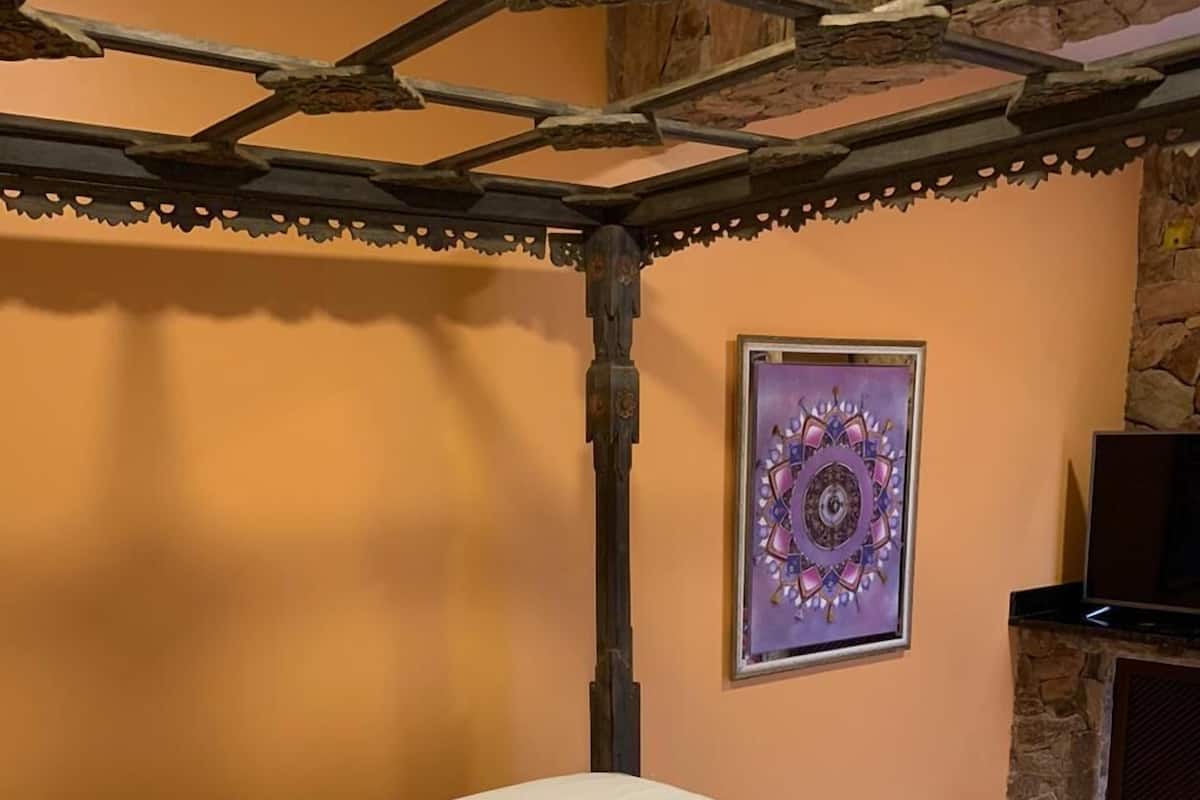 A single bed with a white mattress and quilted pillows in a room with peach walls and a stone accent wall. A framed mandala artwork is on the wall.