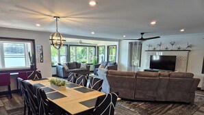 A spacious living room with a large sofa, a dining table with chairs, and a TV mounted on the wall. - Luxurious Lakeside Retreat on Pequawket Lake (Limington)