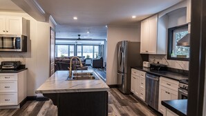 A modern kitchen with a central island, stainless steel appliances, and a view to the living area. - Luxurious Lakeside Retreat on Pequawket Lake (Limington)