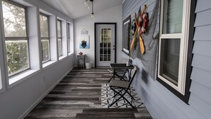 A covered porch with a wooden floor, a table with chairs, and a door with a glass panel. - Luxurious Lakeside Retreat on Pequawket Lake (Limington)