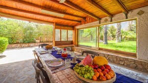 Un espacio exterior para comer con una mesa lista para dos personas, rodeado de muros de piedra y amplias ventanas que dan a un exuberante jardín.