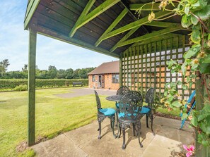 A covered patio with outdoor furniture, a brick building in the background, and a green lawn.