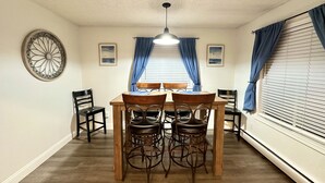 A dining area with a wooden table and four chairs, a ceiling fan, and two windows with blue curtains. - *The Lovely Place* Stunning 3BR 1.5 BA Sleeps 7. Private driveway RV parking.  (Anchorage)