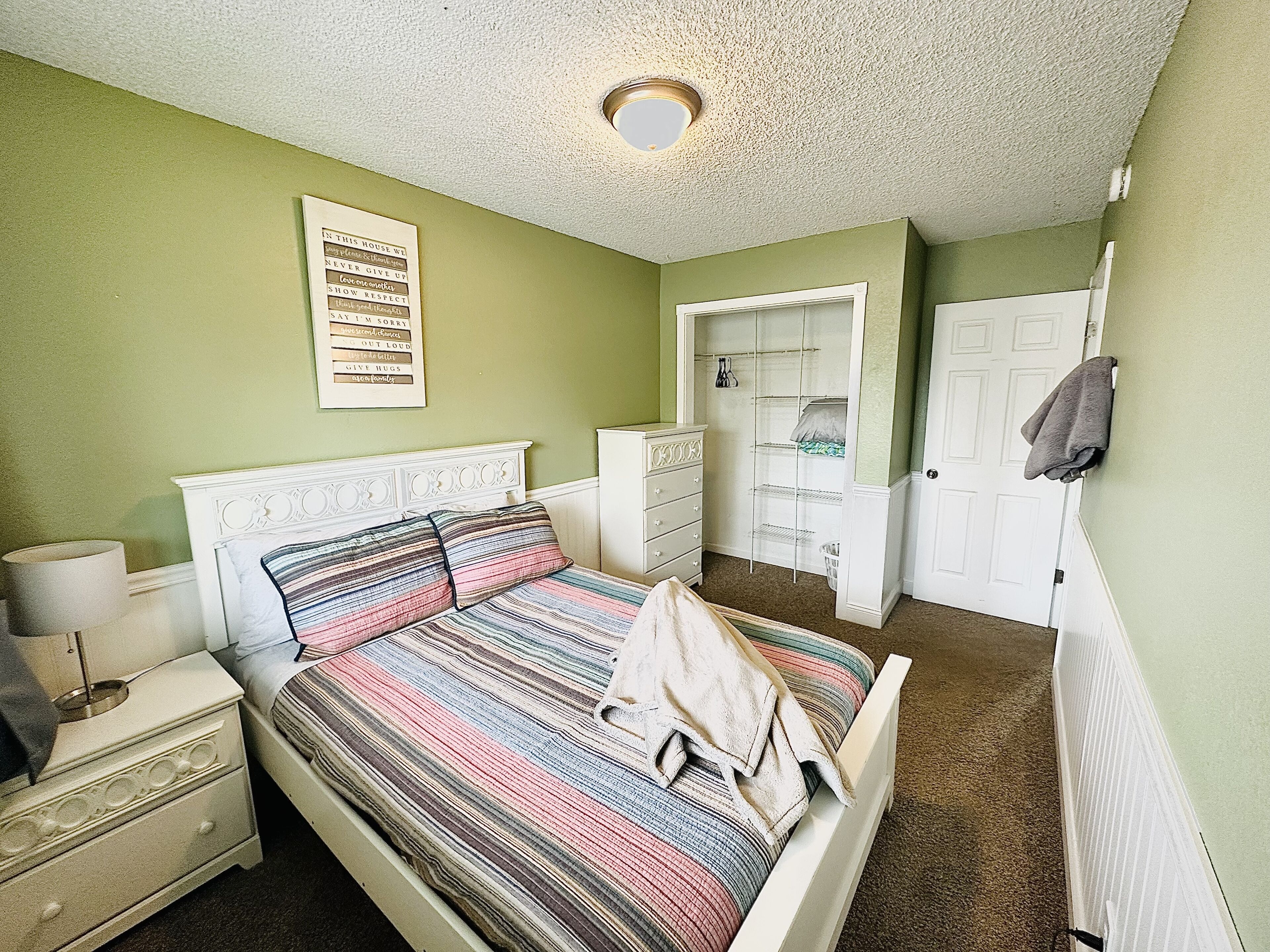 A bedroom with a bed, a nightstand, a dresser, a door, and a wall with a poster.