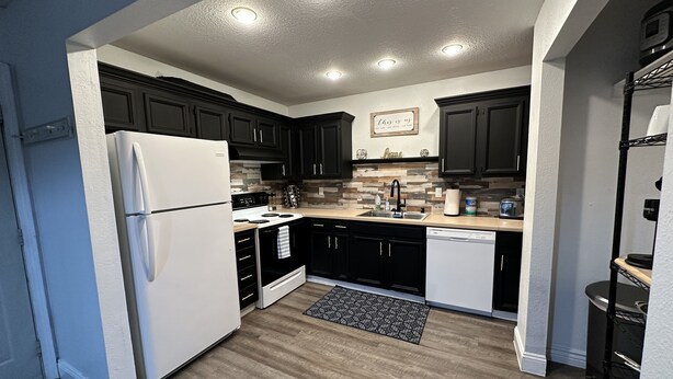 A modern kitchen with dark cabinets, a white refrigerator, a stove, and a dishwasher. - *The Lovely Place* Stunning 3BR 1.5 BA Sleeps 7. Private driveway RV parking.  (Anchorage)