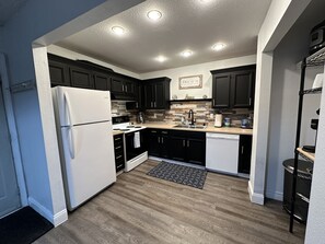 Une cuisine moderne avec des meubles de couleur sombre, un réfrigérateur blanc, une cuisinière et un lave-vaisselle.