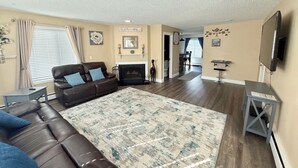 A living room with a brown leather sofa, a patterned rug, a fireplace, and a television mounted on the wall. - *The Lovely Place* Stunning 3BR 1.5 BA Sleeps 7. Private driveway RV parking.  (Anchorage)