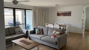 Un saló modern amb un sofà gris, una taula de centre de fusta i un ventilador de sostre.