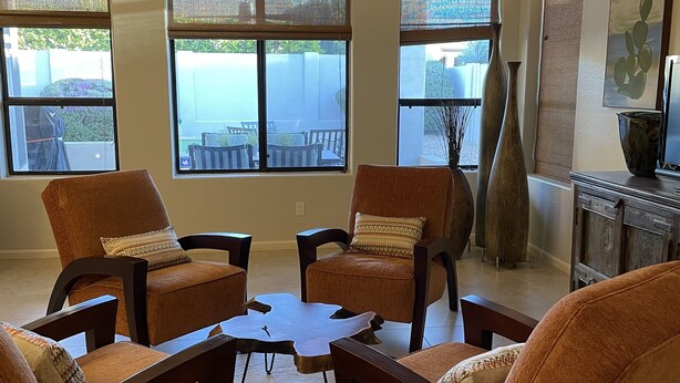 Una sala de estar con cuatro sillones de cuero marrón, una mesa de centro y ventanas amplias con persianas.