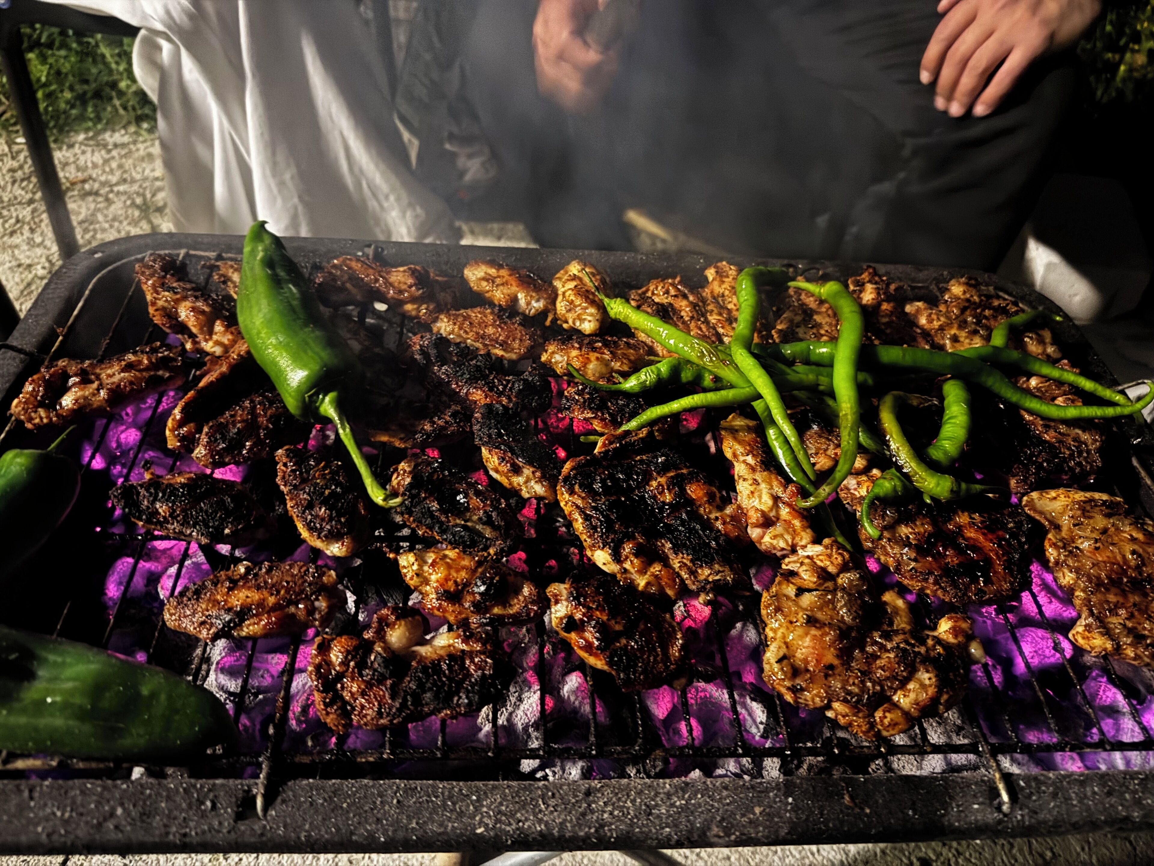 A grill with various meats and green peppers being cooked.