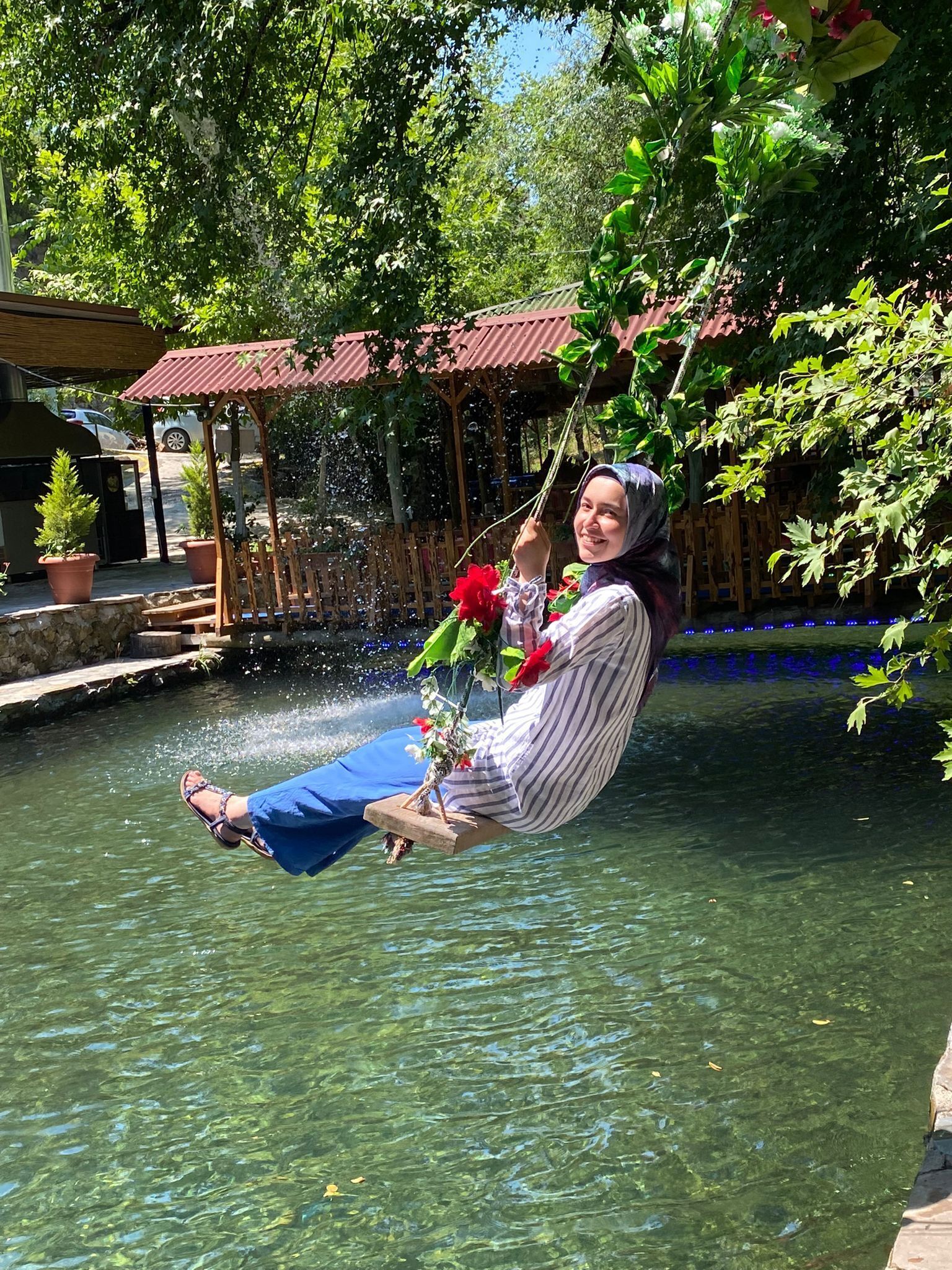 Eine Person sitzt auf einer Schaukel über dem Wasser und hält eine rote Blume.