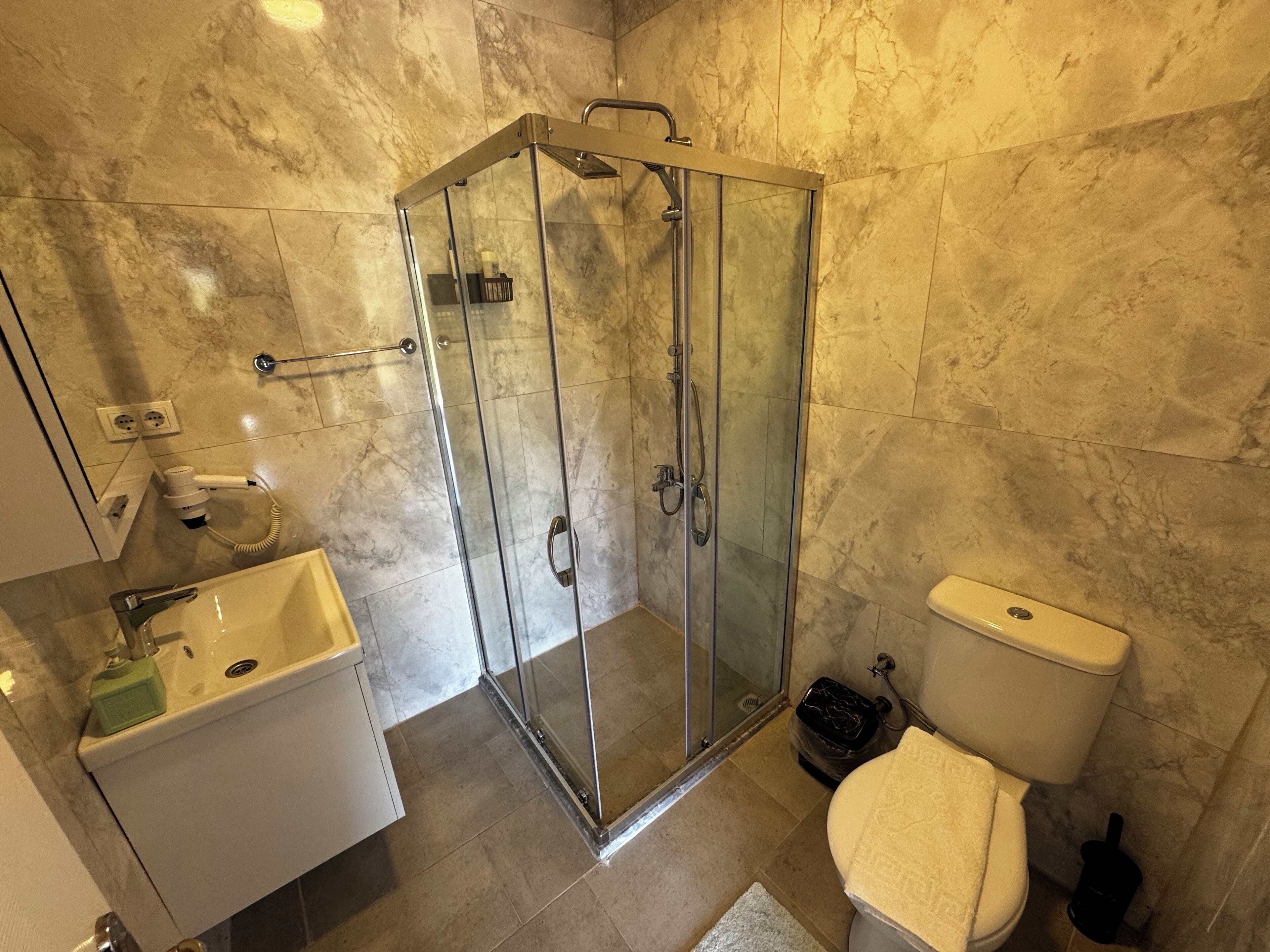 Un baño con ducha de vidrio, un lavamanos blanco y un inodoro.