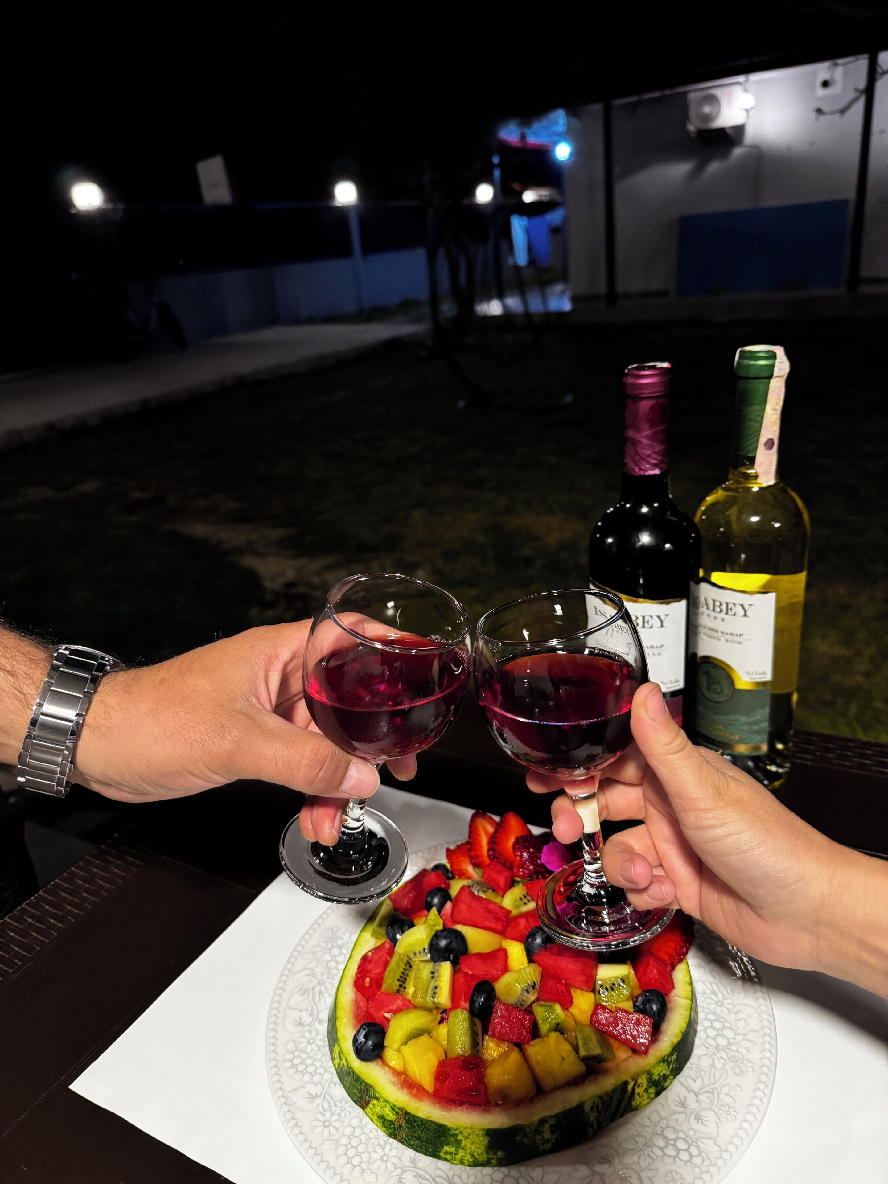 Une table avec deux verres à vin remplis de vin rouge, une bouteille de vin et une salade de fruits à base de pastèque.