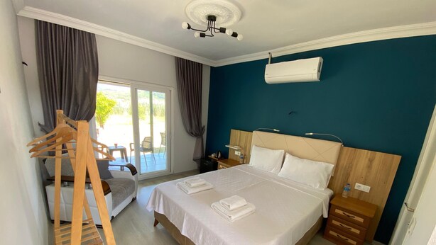 A hotel room with a bed, a wooden chair, a desk, a nightstand, and a ceiling fan. - Dalaman Airport Guesthouse (Dalaman)