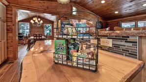 A wooden interior with a kitchen counter holding snacks and a fruit basket. - Log home mins from Lake George, w/ heated salt water pool and hot tub! (Warrensburg)