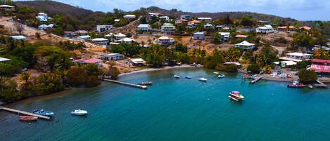Uma vila costeira com casas numa encosta, um cais com barcos e águas turquesa cristalinas.