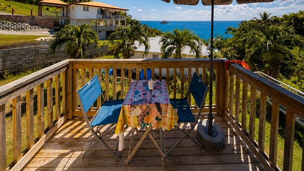 Een houten terras met een tafel, stoelen en een grote parasol, met uitzicht op de oceaan.