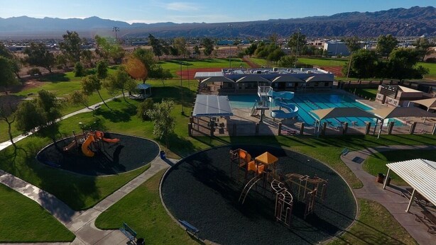 Un parque infantil con dos zonas de juego circulares, una piscina y un edificio con porche cubierto.