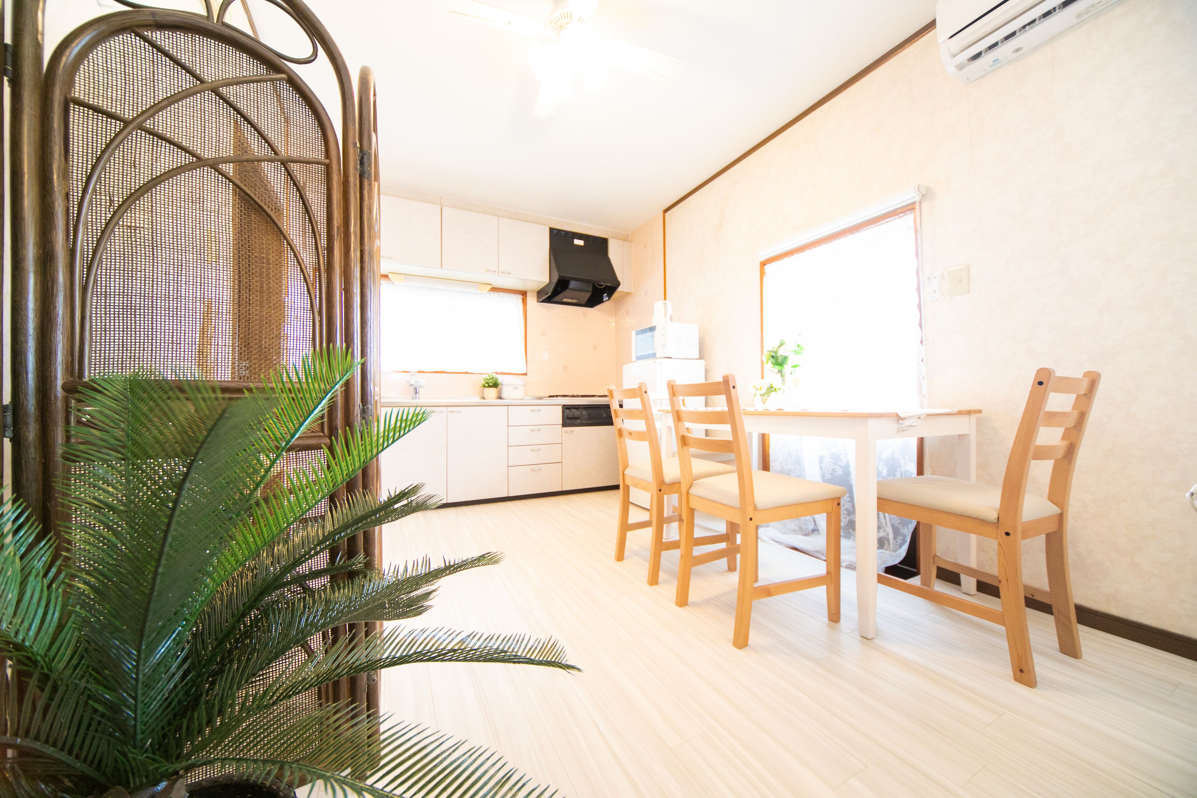 Une cuisine compacte avec des meubles blancs, une table à manger avec des chaises et une grande fenêtre qui laisse entrer la lumière naturelle.