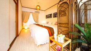 Habitación de hotel con cama, mesita de noche con un jarrón de flores, ventana con cortinas y una planta.
