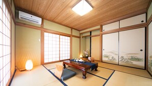 Una habitación japonesa tradicional con suelo de tatami, una mesa de madera baja, un banco acolchado, puertas correderas y un ventilador de techo.
