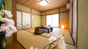 Una habitación tradicional japonesa con suelo de tatami, una mesa baja, un sofá, puertas correderas y vistas al exterior.