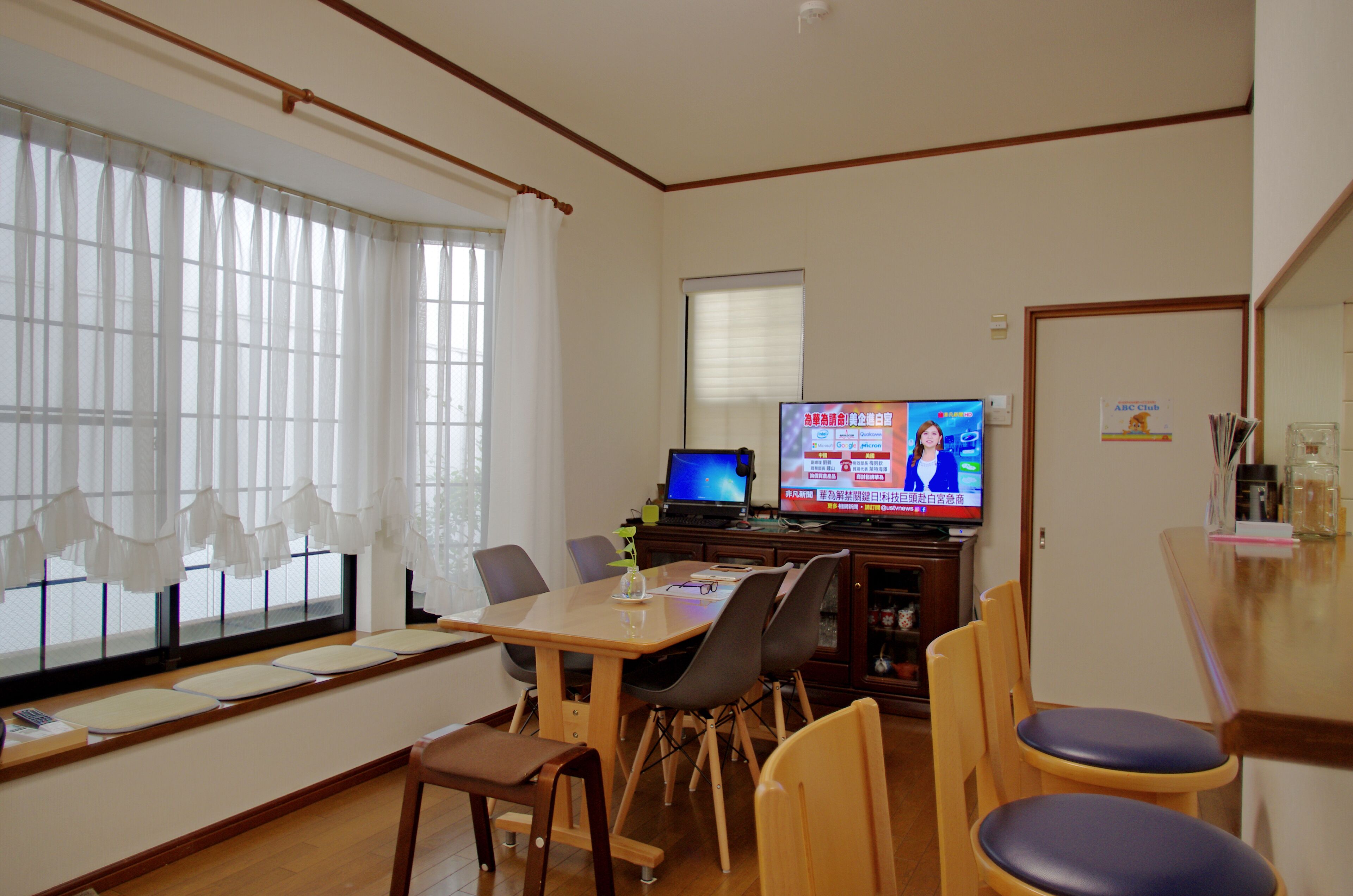 A dining area with a wooden table, chairs, and a television displaying a news program.