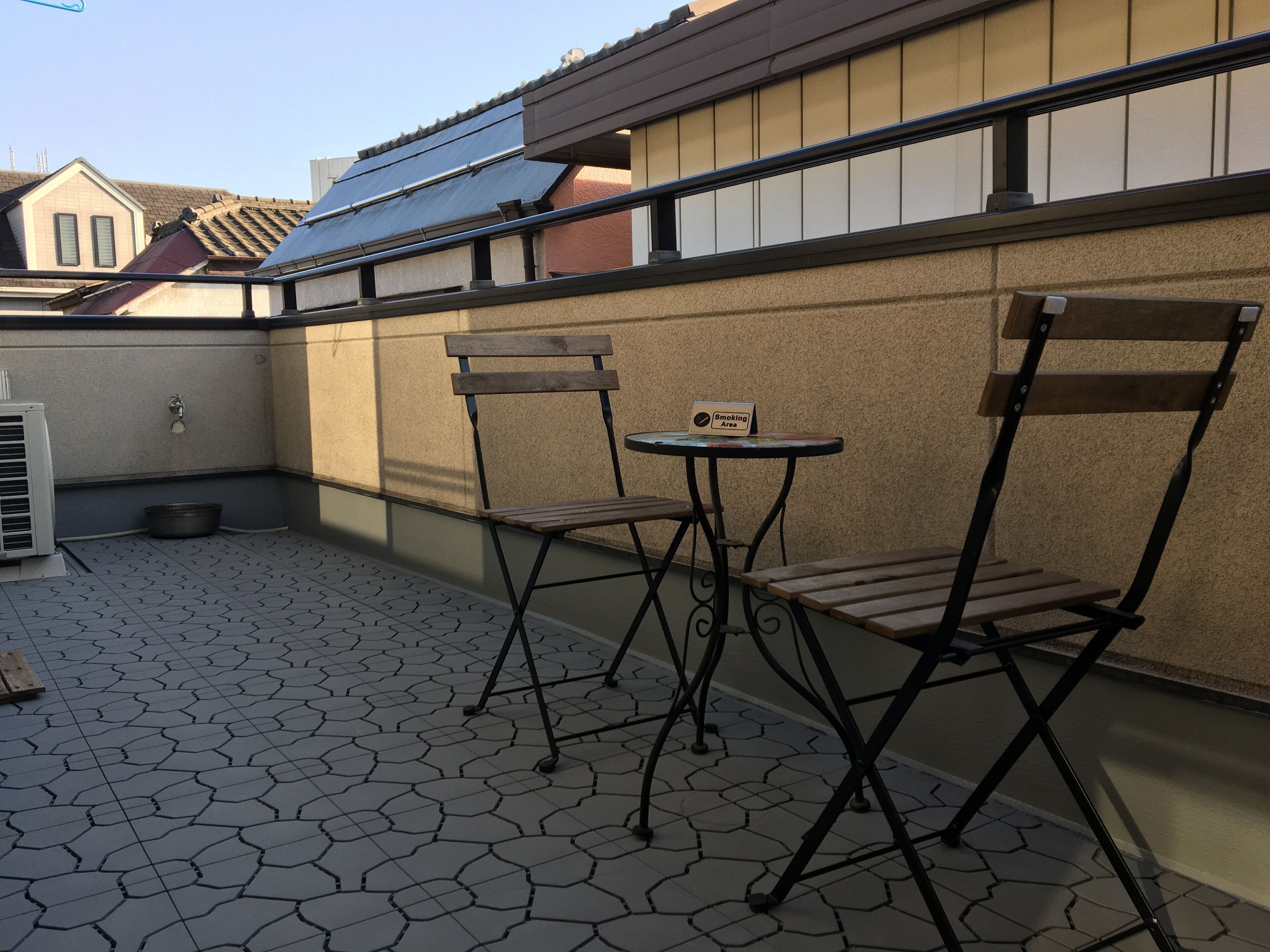A patio area with hexagonal tiles, two wooden chairs, a small round table, and a "Smoking Area" sign.