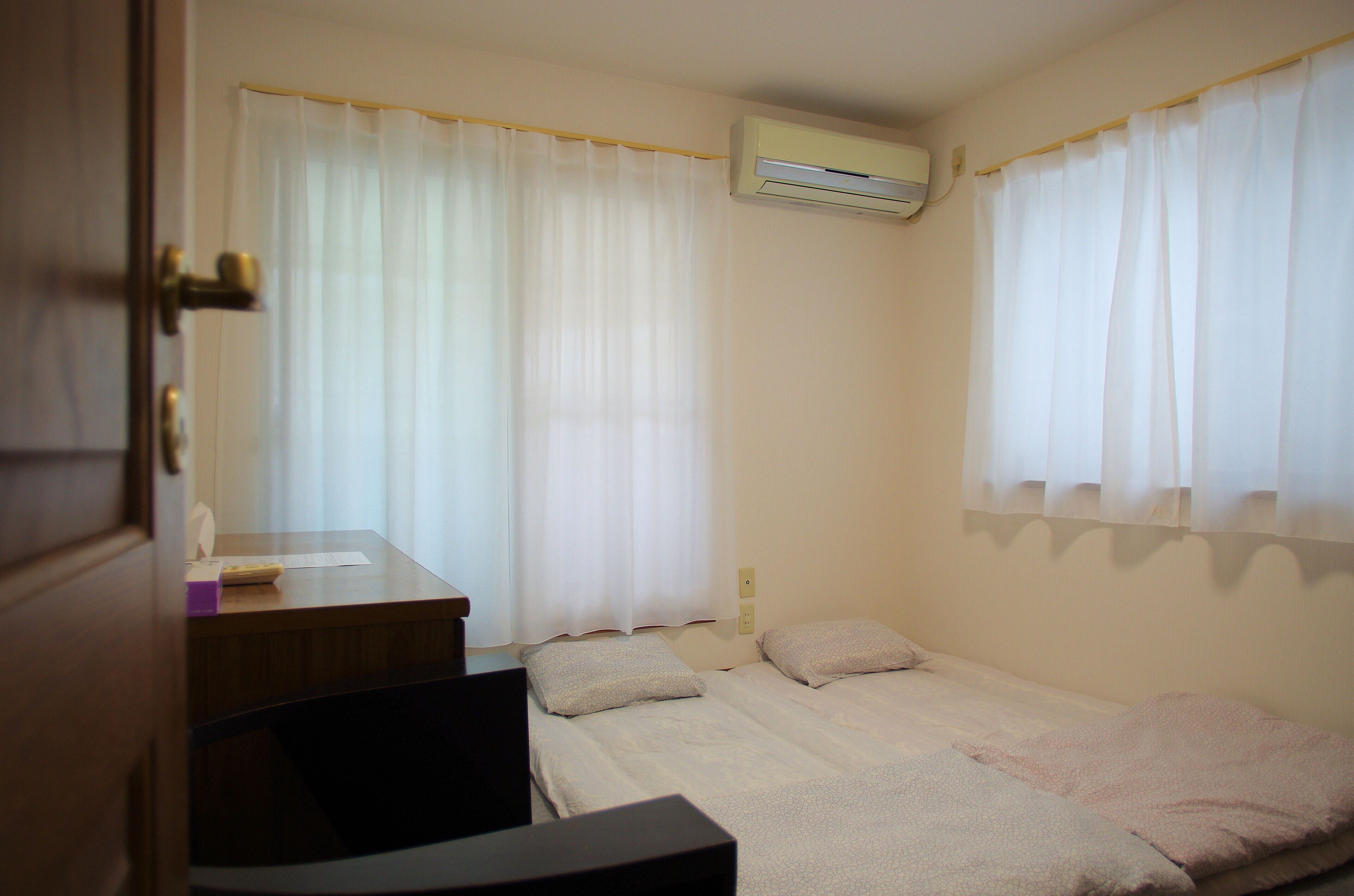 A small, clean room with two beds, a desk, and an air conditioning unit.
