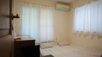 A small, clean room with two beds, a desk, and an air conditioning unit.
