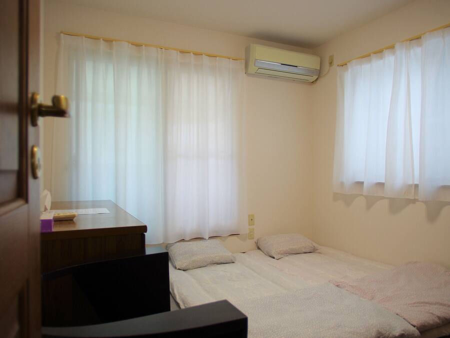 A small, clean room with two beds, a desk, and an air conditioning unit.