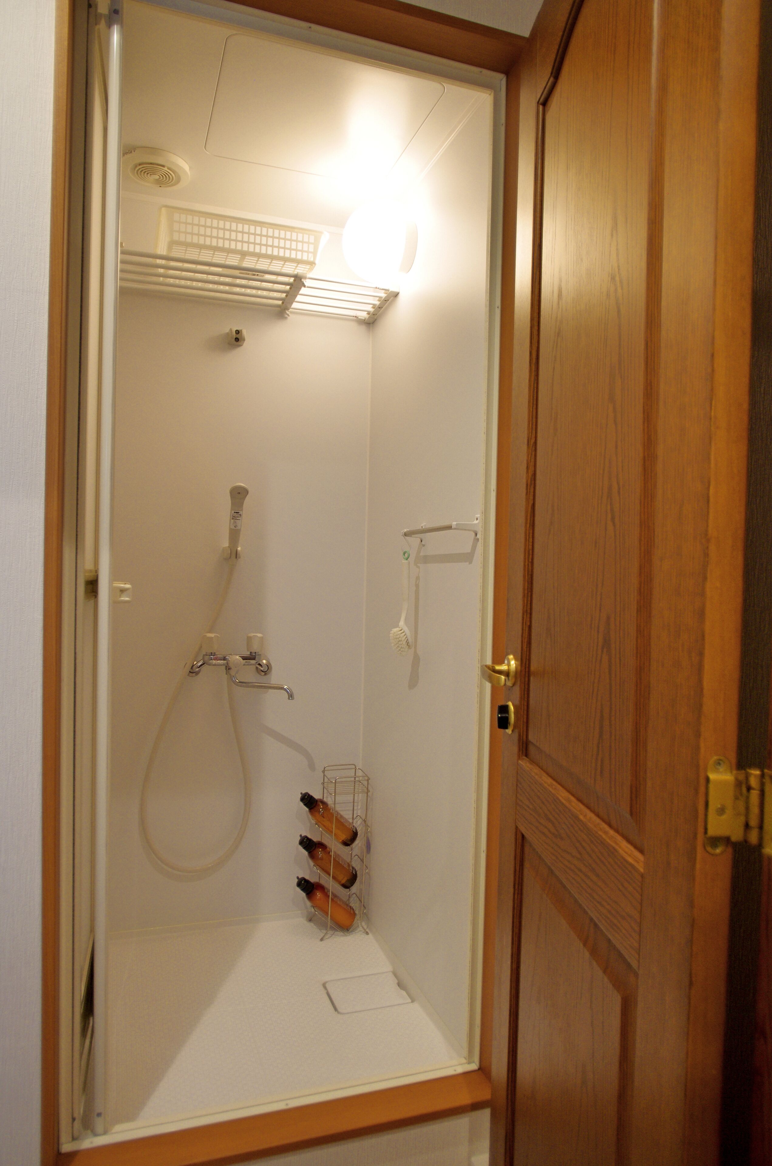 A small, enclosed shower area with a wooden door, a towel rack, and a bottle holder.