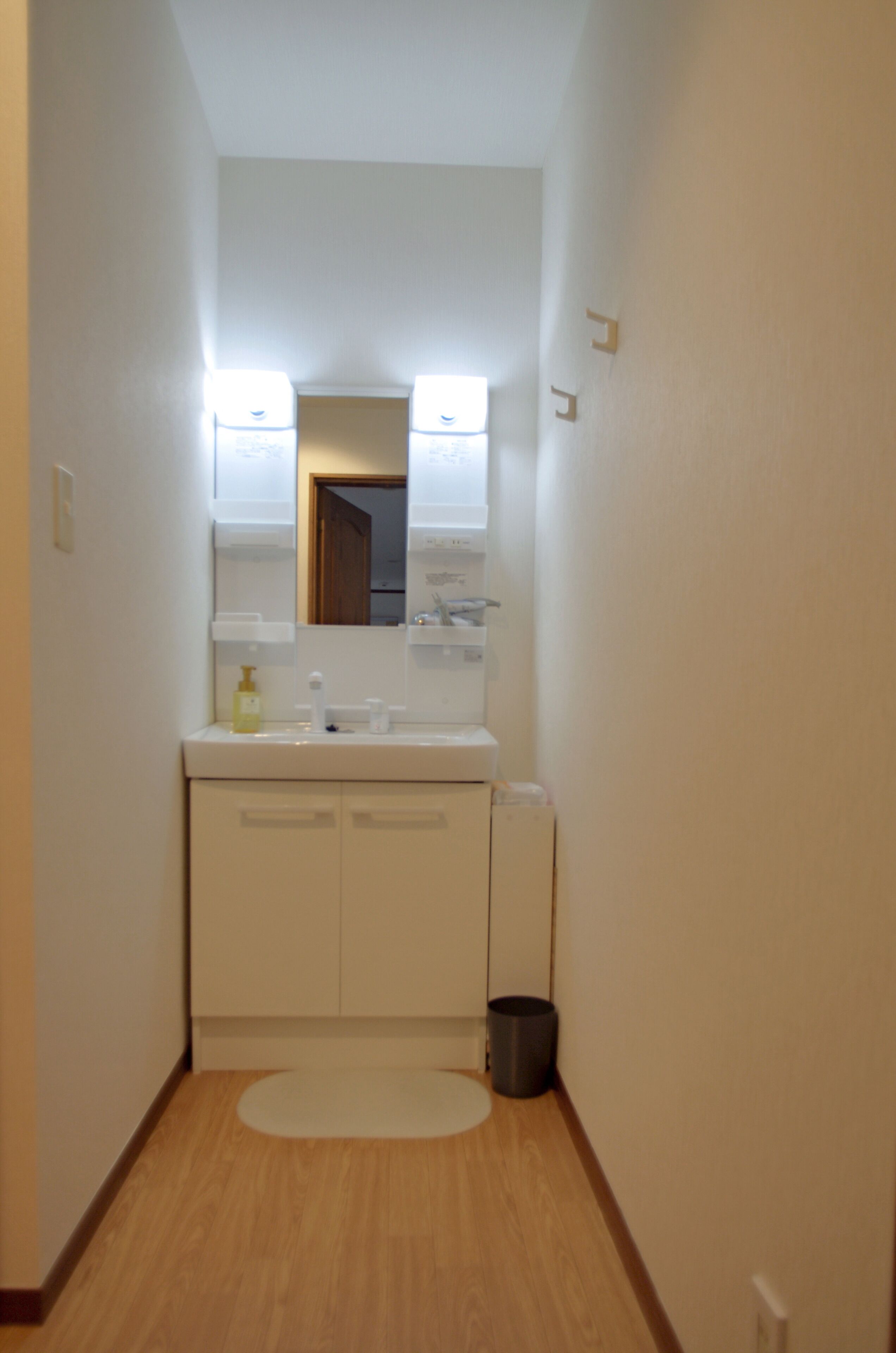 A narrow hallway with a white sink, mirror, and cabinets.