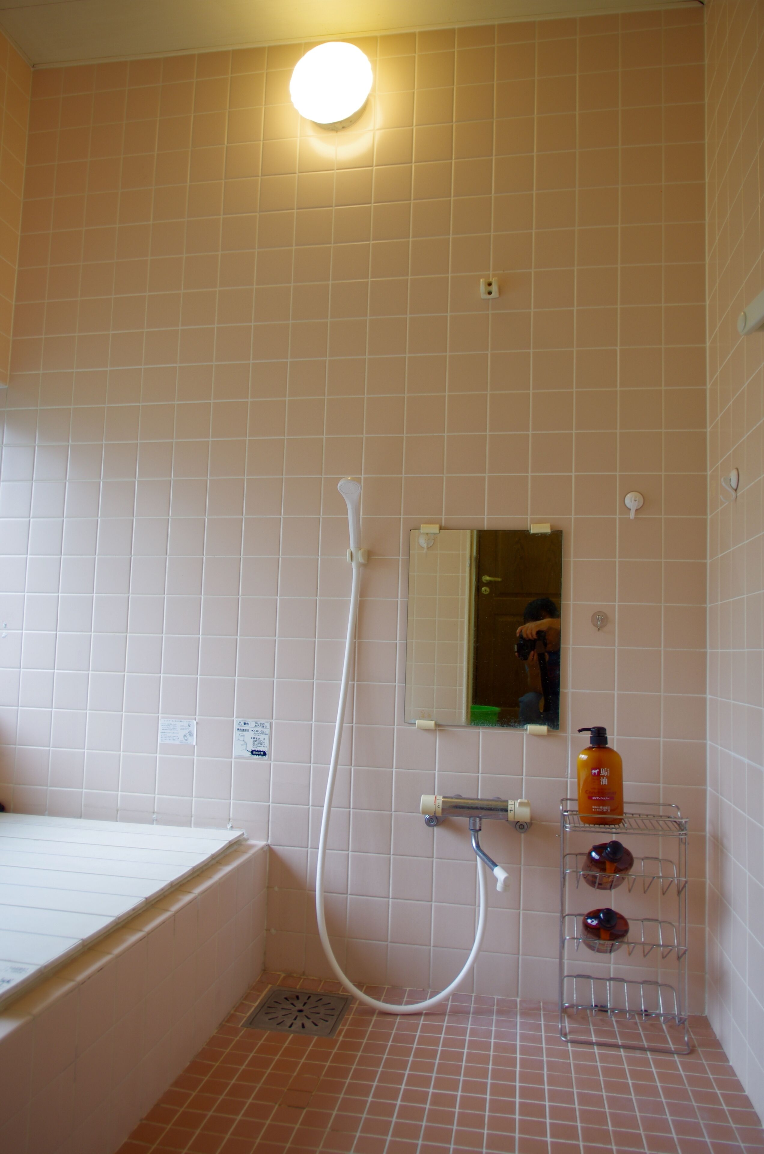 A bathroom with a bathtub, a shower, a mirror, and a shelf with toiletries.