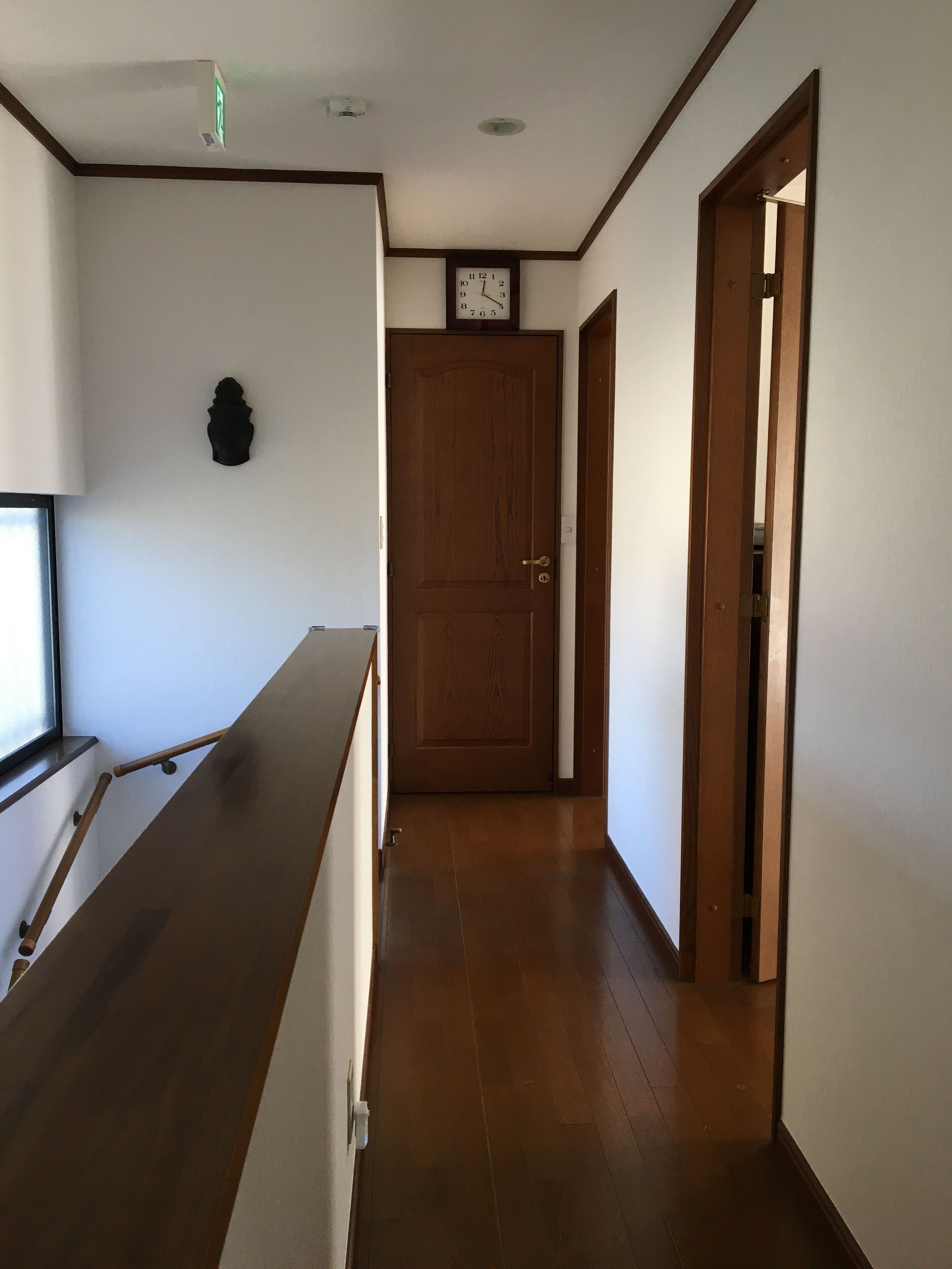 A hallway with wooden flooring, a clock on the wall, and a door at the end.